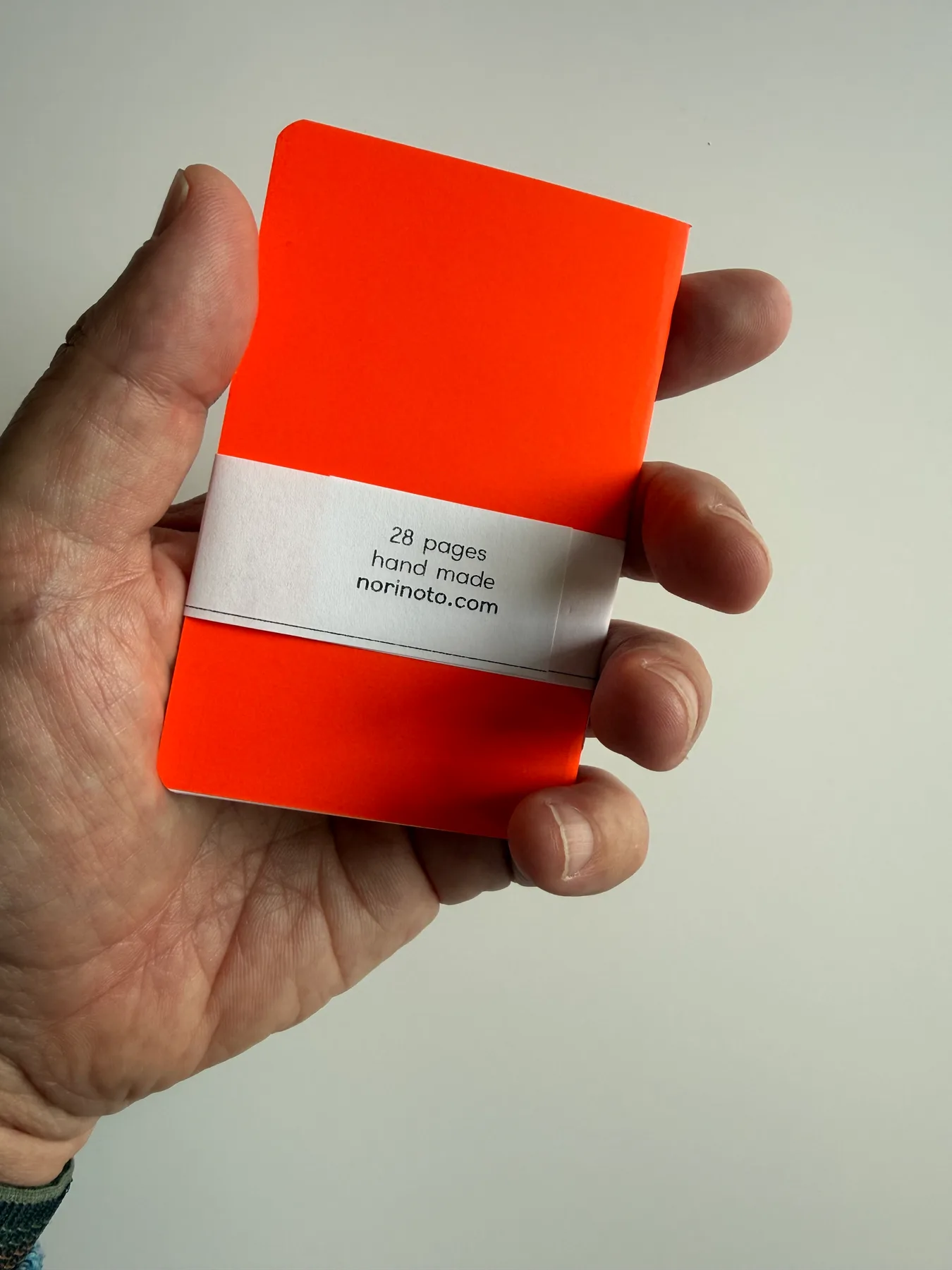 Back of a fluorescent orange Mīnī Neō notebook held in one hand