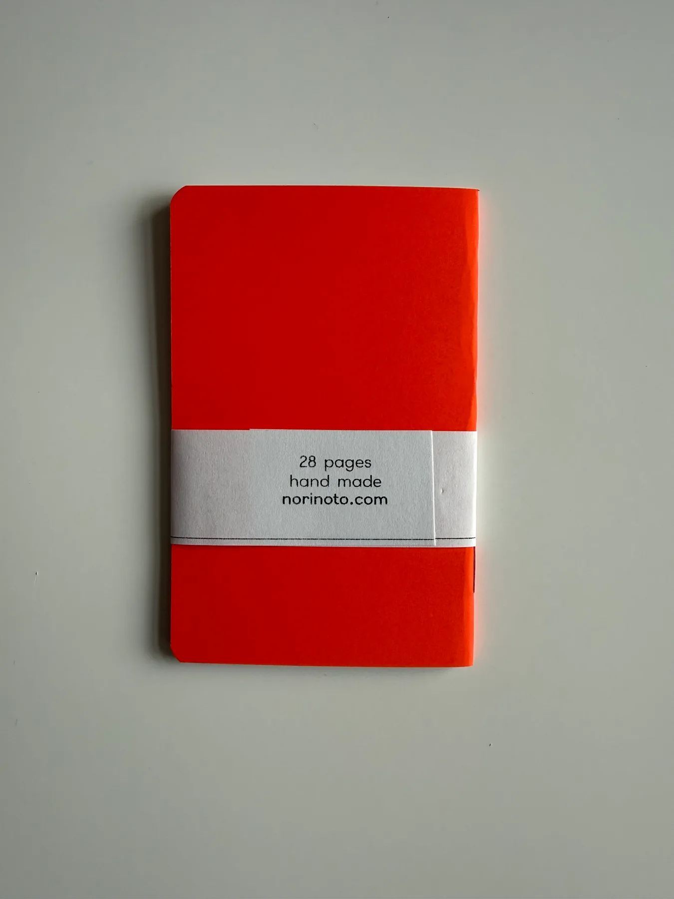 Back of a fluorescent orange Mīnī Neō notebook showing its handmade label