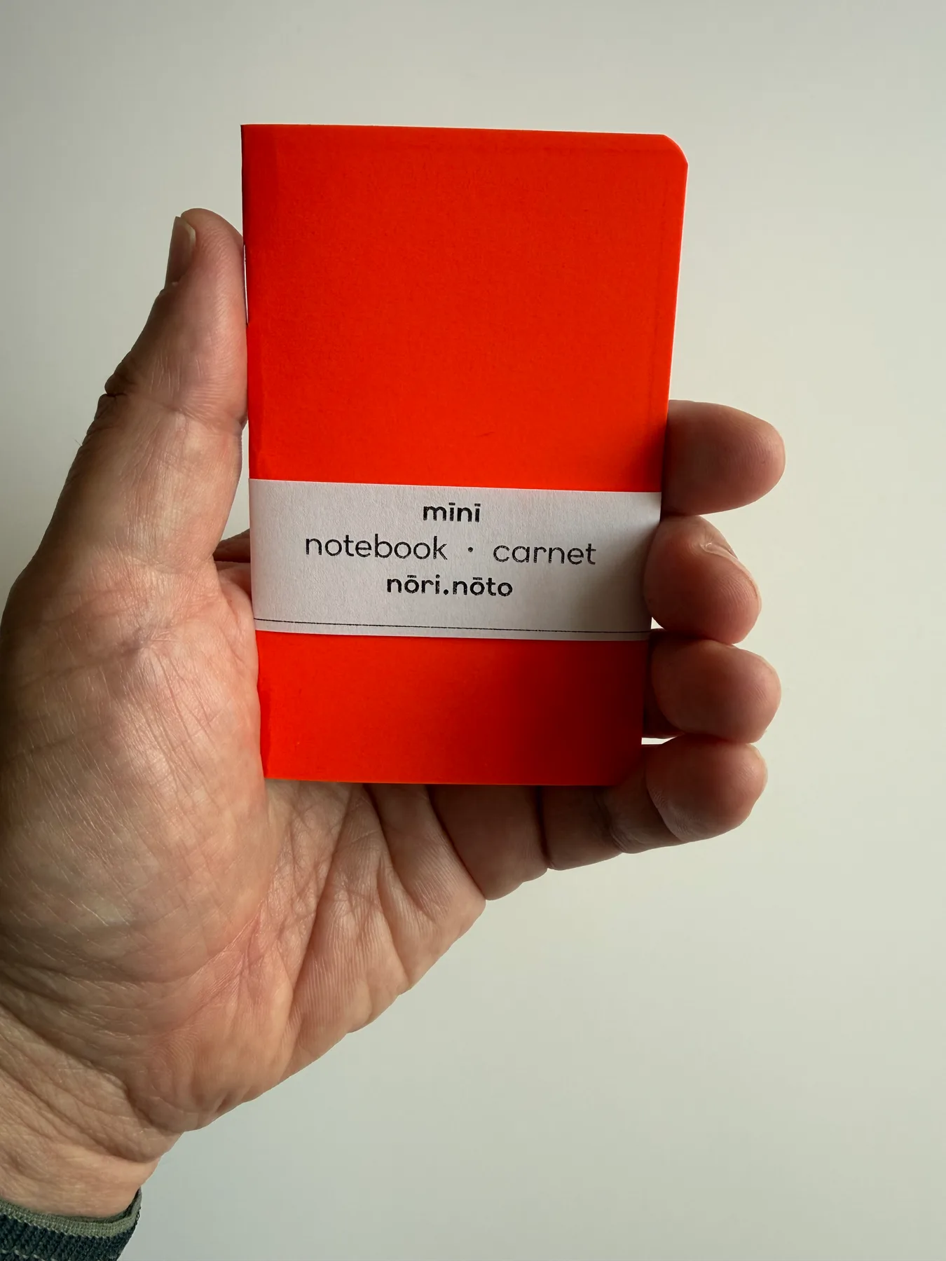 Fluorescent orange Mīnī Neō notebook held in one hand