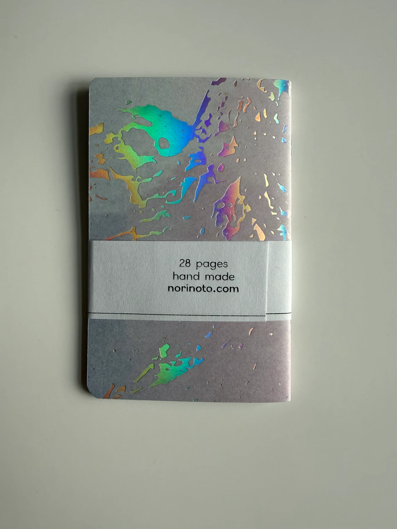Back of a holographic creative-paper Mīnī notebook showing its handmade label