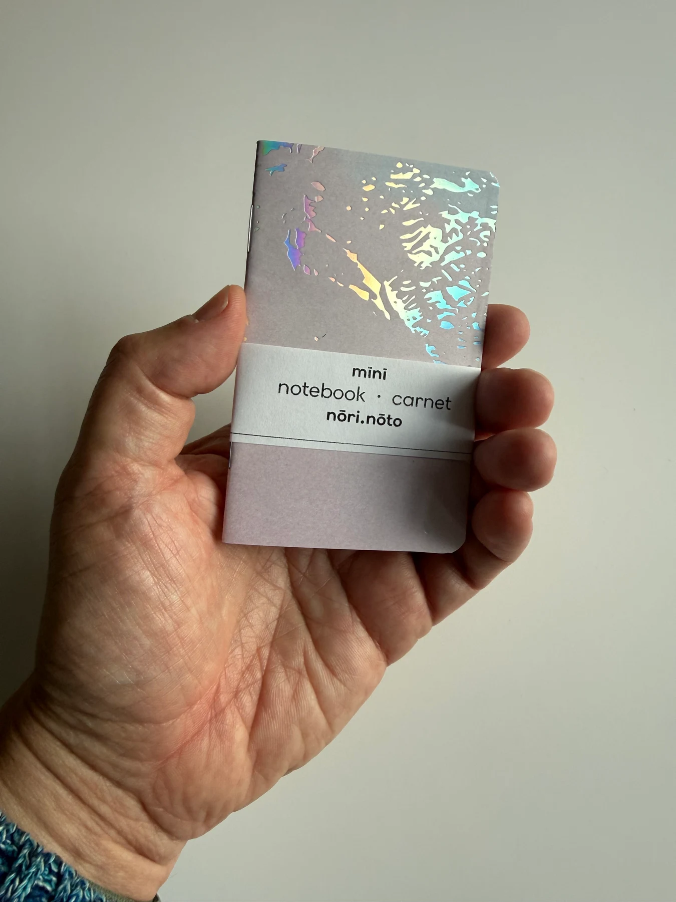 Grey holographic Mīnī notebook held in one hand to show its pocket size