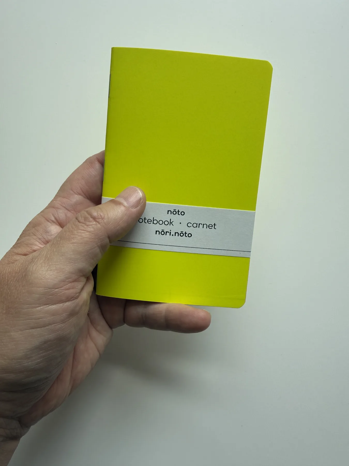 Fluorescent yellow Nōto Neō notebook held in one hand