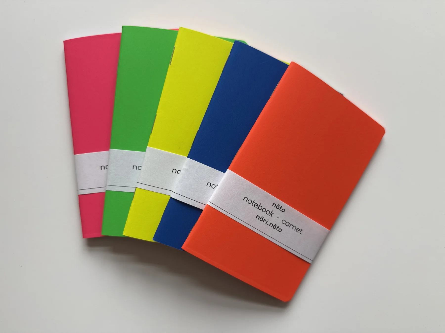 Five Nōto Neō notebooks in fluorescent pink, green, yellow, blue, and orange